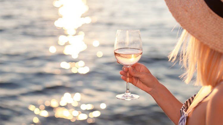 Someone holding a glass of wine with the sea in the background