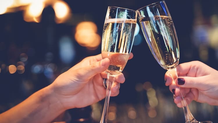 Two glasses with sparkling champagne being cheersed by people celebrating