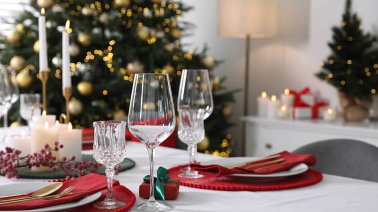 A dining table set for dinner with a Christmas tree in the background